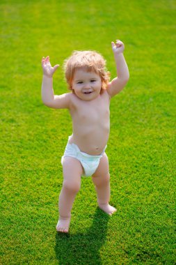 Çocuklar büyüyor. Sahada çimenlikteki mutlu bir bebek yaz akşamı bebek bezi takıyor. Dışarıda gülümseyen bir çocuk. Aile hayatında mutluluk ve uyum..