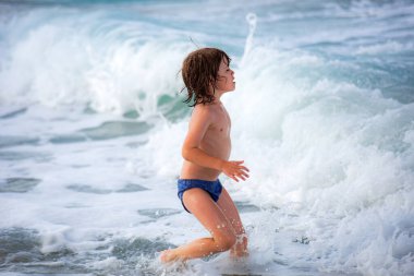 Çocuk yazın mavi denizde oynuyor ve kumsalda eğleniyor. Dalgalı mavi okyanus. Çocuk denizde yüzüyor..