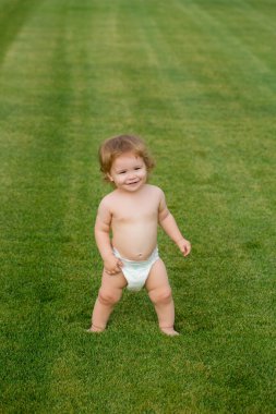 Yaz akşamında çimlerin üzerinde mutlu bir bebek. Dışarıda gülümseyen bir çocuk. Mutlu çocukluk ve çocuk sağlığı hizmetleri.