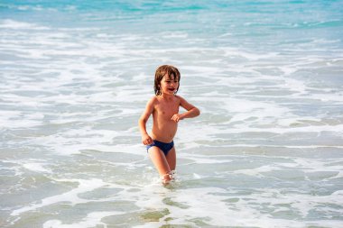 Çocuk yaz tatilinde plajda oynuyor. Doğada çocuklar ve güzel deniz. Mutlu çocuklar deniz kenarında tatildeler, suda koşuyorlar..