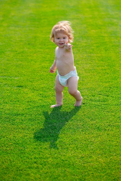 Bonito menino engraçado aprendendo a rastejar passo, se divertindo jogando no gramado no jardim em calças de fraldas. — Fotografia de Stock