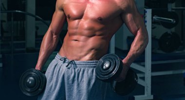 Jimnastik reklamı. Altı paketli erkek gövdesi. Dambıllarla antrenman.