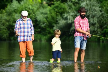 Baba ve büyükbabasıyla birlikte çocuk nehir dibinde açık havada balık tutuyor. Balıkçılık popüler bir eğlence aktivitesi haline geldi..