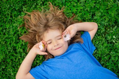 Çocuklar bahar parkında eğleniyor. Çocuk yeşil çimlerin üzerinde yatıyor. Üst görünüm portresi