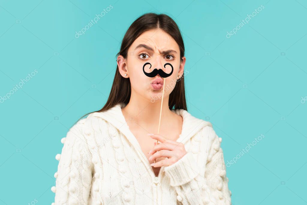 Surprised winking model Girl holding funny mustache on stick and showing empty copy space on open hand palm for text, white background. Girl presenting point. Proposing product. Advertisement gesture