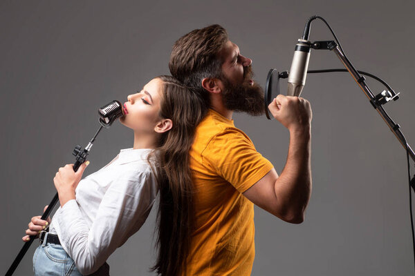 Boy and girl with excited faces enjoy music. Couple in recording studio. Music performance vocal. Singer singing song with a microphone.