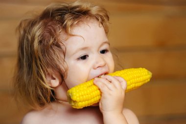 Bebek sarı mısır yiyor ya da mısır yiyor ve tahta arka planda komik bir yüz var..