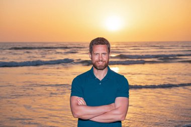 Deniz manzarasında poz veren tişört giyen yakışıklı bir adam. Sahilde yaz tatilinin tadını çıkaran neşeli bir adamın portresi..