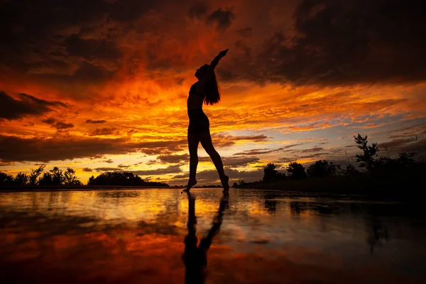 Black silhouette of pretty girl or beautiful woman, sexy slim model, with long hair poses on sea beach at sunset outdoors on violet sky background