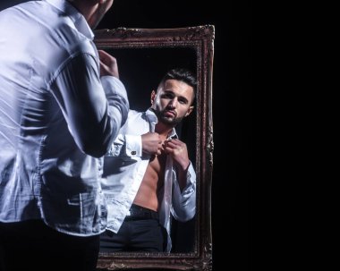 Seksi vücutlu sporcu ya da sporcu ciddi yüzlü, siyah arka planda izole edilmiş klasik aynanın yanında beyaz gömlekli çıplak vücutlu..