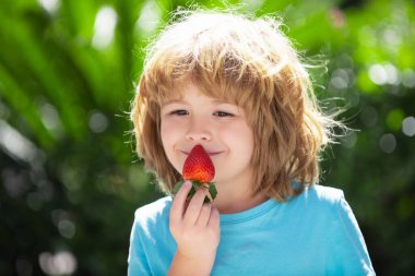 Sağlıklı çocuk yemekleri. Yeşil yaz geçmişinde çilek yiyen şirin küçük çocuk. Mutlu yüzlü çocukları kapatın..