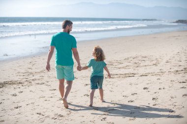 Baba ve oğul denizde yürüyor. Baba ve çocuk el ele tutuşup birlikte yürüyorlar. Yaşam tarzı ve aile tatili, mutluluk adamı konsepti..