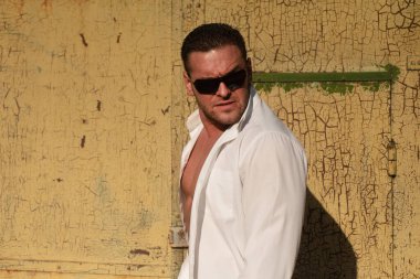 Kendine güvenen maço adam. Erkek vahşi tarzı. Beyaz gömlekli ve güneş gözlüklü çekici bir adam..