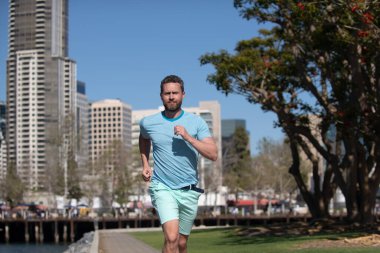 Erkek koşucu güzel bir yaz gününde şehirde koşuyor..