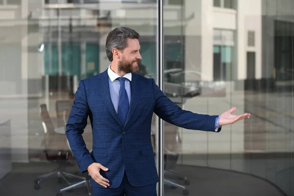 Retrato de empresario positivo cerca del entorno corporativo moderno. Hombre de negocios joven guapo mirando al aire libre con el edificio de oficinas en el fondo. —  Fotos de Stock
