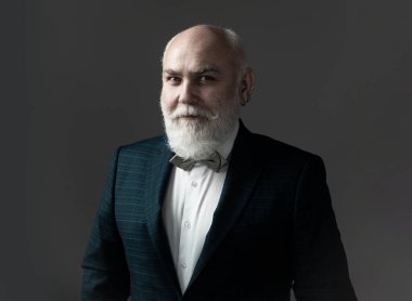 Takım elbiseli ve kravatlı kendinden emin yaşlı sakallı adam gri izole arka planda duruyor. Moda kıyafetli yetişkin adam pozu.