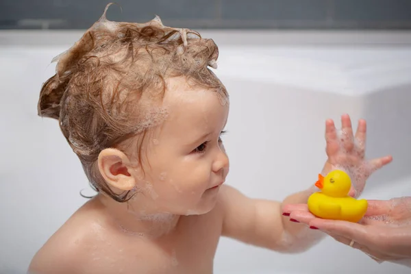 Babywäsche in einem Badezimmer in Schaumstoff. Kinderschaumbad. Lächelndes Kind im Badezimmer mit Spielzeugente. — Stockfoto