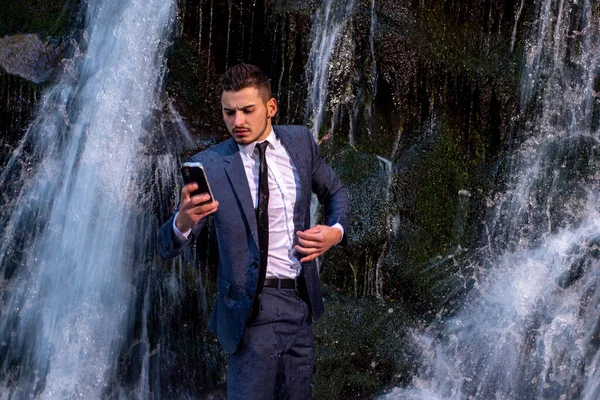 Obchodník se zařízením na dálkové práci. Obchodní muž v obleku držení notebook na vodopádu venkovní pozadí. — Stock fotografie