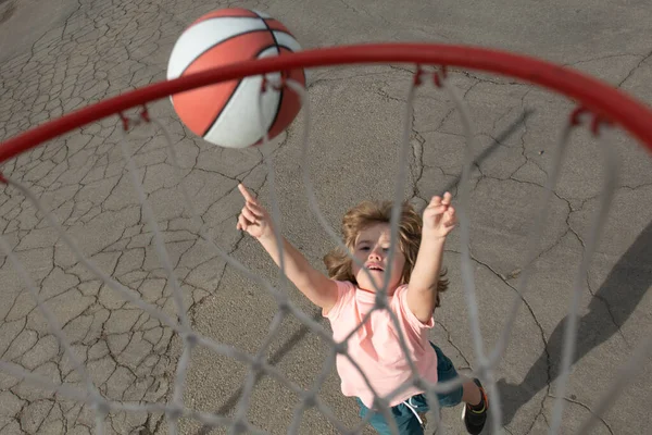 Ragazzino carino in uniforme da basket che salta con pallone da basket per sparare. Felice bambino che gioca a basket nel parco giochi. — Foto Stock