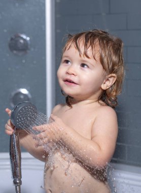 Duşun altında yıkanan çocuk. Banyo yapan bebek. Kafasında köpük olan mutlu çocuk..