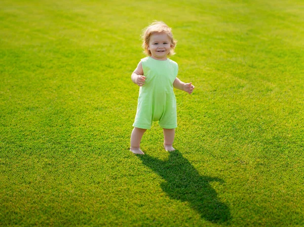 小さな赤ちゃんは草の上に手順をクロールすることを学ぶ。コンセプトの子供の月。緑の芝生の遊び場で遊ぶ幸せな子供。第一歩. — ストック写真