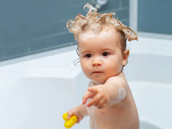 Lustiger blonder Junge, der Spaß mit Wasser hat, indem er in der Badewanne badet. Badendes Baby. Glückliches Kind mit Seifenschaum auf dem Kopf. — Stockfoto