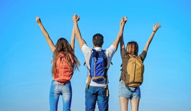 Güneşli bir günde sırt çantalı arkadaşlar mavi gökyüzü arka planında el kaldırıyorlar. Dertsiz mutluluk özgürlüğü kavramı. Doğada turistler.