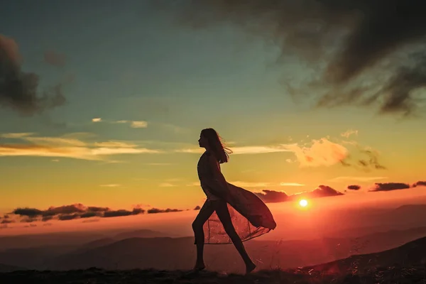 Žena kráčí na krásný výhled na západ slunce nebo východ slunce na modré obloze s mraky. Silueta na přírodním pozadí. — Stock fotografie