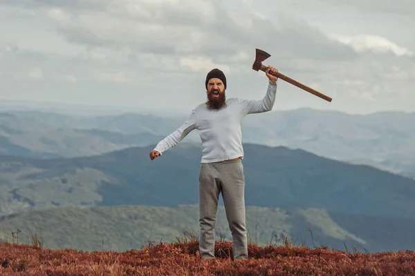 Un bell'uomo barbuto con l'ascia. Brutale boscaiolo hipster con barba e baffi cavalletti con ascia sulla cima della montagna. — Foto Stock