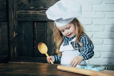 Mutfakta aşçı şapkası ve önlüğü var. Ev yapımı pişirme ve pişirme. Çocuk masada kaşık, merdane ve makas kullanıyor..