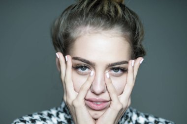 Kız uzun narin parmaklarıyla yüzüne dokunuyor. Gri arka planda büyük yeşil gözlü ve gür kirpikli güzel bir kadının portresi..