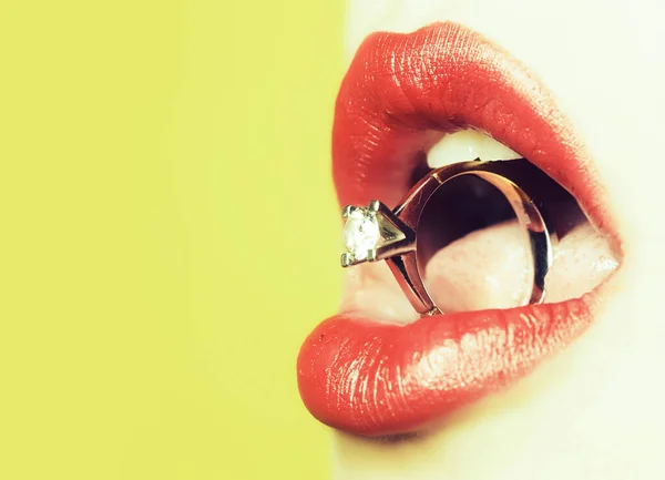 Detailní záběr na ženské sexy rty s červeným rtěnkou drží kulatý zlatý prsten jako dárek s klenotem v otevřených ústech s jazykem. — Stock fotografie