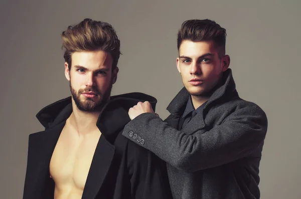 Los hombres amigos en los abrigos, tiene el pelo a la moda y la cara seria sobre el fondo gris. Elegante sexy chicos en estudio con torso desnudo. —  Fotos de Stock