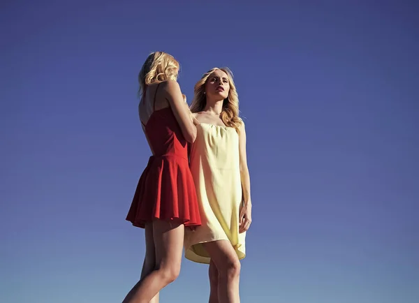 Mulheres gêmeas com cabelo loiro e pernas sensuais longas no verão no fundo do céu azul, família e irmãs, beleza e moda, liberdade. — Fotografia de Stock