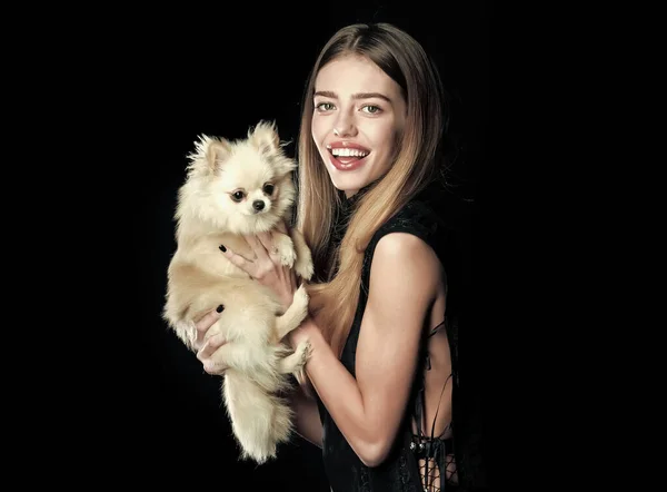 Gitl with dog, woman play with pet. Pet at woman isolated on black background. Girl with happy face and long hair hold puppy. Beauty and fashion. Woman with small dog of Pomeranian spitz, copy space. — Stock Photo, Image