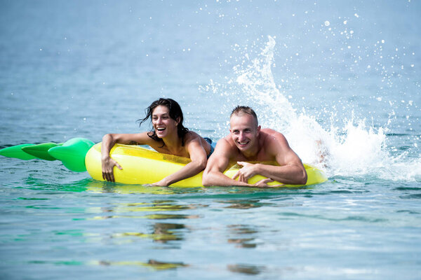 Happy young couple swimming and laughing on air mattress. Couple vacation concept. Man and woman on honeymoon, swim on pineapple shaped mattress in sea. Summer accessories for rest.