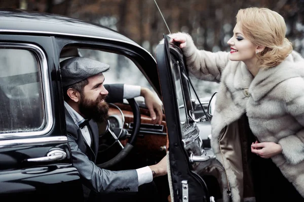 Condutor com mulher de casaco de peles. Casal vintage no carro retro preto. — Fotografia de Stock