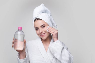 Beautiful woman delicately moisturizes skin with cosmetic tonic. Portrait of lady with healthy skin without makeup on isolated background. Micellar water. clipart