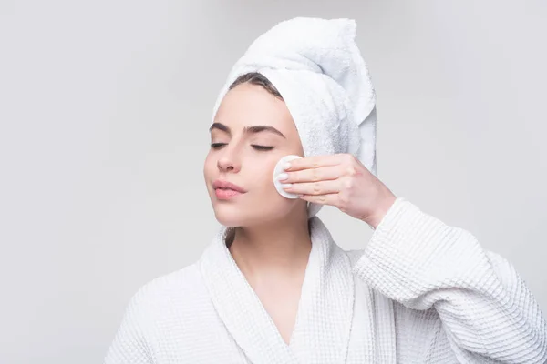 Primer plano de la hermosa joven lavándose la cara con la almohadilla de algodón sobre el fondo gris. Los ojos están cerrados. —  Fotos de Stock