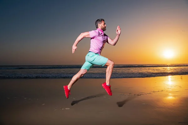 Homme courant sur la plage au coucher du soleil. Un joggeur qui court. Mouvement de saut dynamique. Saut sportif. — Photo