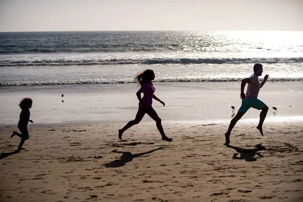 Silhouette di famiglia che fanno jogging lungo la spiaggia al sorgere del sole. Allenamento all'aperto, silhouette di corridori, sport e stile di vita familiare sano. — Foto Stock