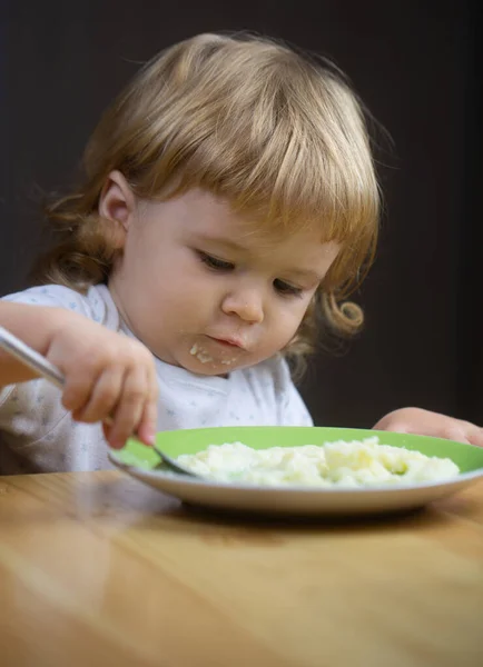 Jedzenie dzieci, koncepcja odżywiania. Cute baby face z łyżką i talerz w kuchni w domu. — Zdjęcie stockowe