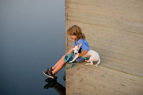 Funny child playing with her puppy dog in the park near lake. Carefree childhood. Protection domestic animal. — Stock Photo, Image