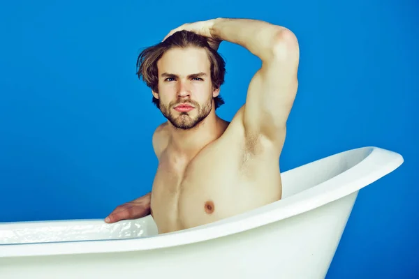 Young man with muscular body sitting in bath tub. Sexy man beauty, relax and hygiene, healthcare, copy space.