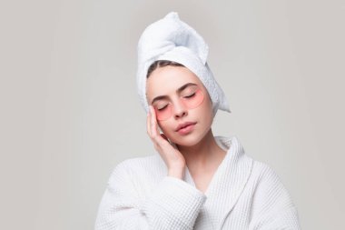 Göz bandı takan bir kadın. Kafasında havluyla portre kızı yakın plan. Şehvetli kız göz torbasını küçültür. Yüz kolajeni cilt estetiği. Nemlendirici cilt. Anti-yorgunluk maskesi takılıyor.