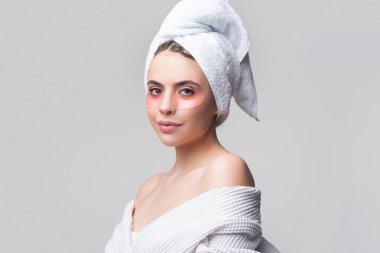 Göz bantlı güzel kadın mükemmel bir cilt etkisi gösteriyor. Gri stüdyoya izole edilmiş yüz bantlarına başvuran çekici genç bir kadının portresi..