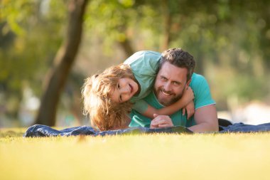 Baba ve çocuk dışarıda kucaklaşıp sarılıyorlar. Baba ve oğul yaz parkında çimlere uzanmış dışarıda vakit geçiriyorlar..