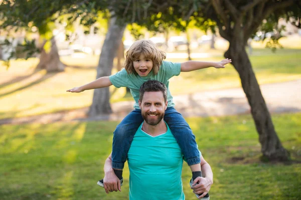 Szczęśliwy ojciec ujeżdżający ramiona w ogrodzie. Syn na ramieniu, tata patrzący w kamerę. Weekendowa aktywność szczęśliwa koncepcja stylu życia rodziny. Wakacje rodzinne. — Zdjęcie stockowe