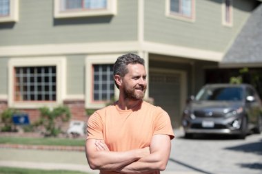 Çapraz kollu yakışıklı bir adamın portresi. Yeni evin önünde dikilip bakıyor..