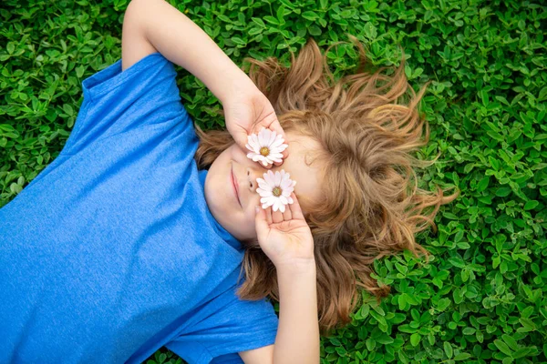 Kinderen hebben plezier in het voorjaarspark. Kind liggend op groen gras. Bovenaanzicht portret. — Stockfoto